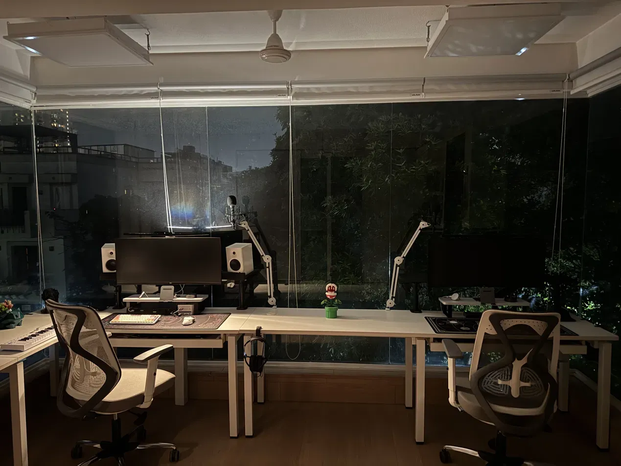 The desk head-on at night, city and greenery through the glass